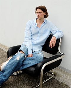 Homme assis portant une chemise bleu clair avec un jean | Atelier Tuffery